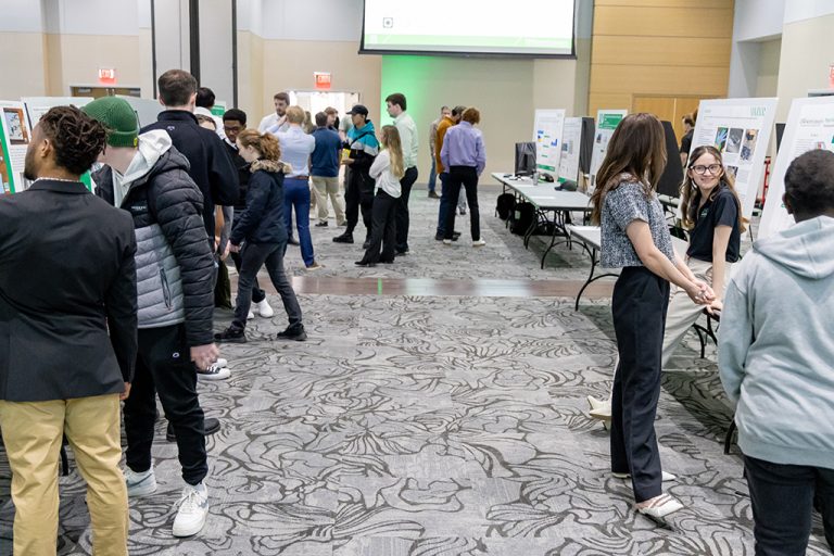 Visitors smile and observe projects presented by students on design posters.