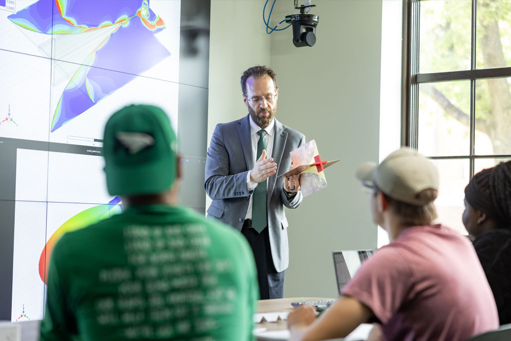 A faculty member gestures to a piece of hardware as he lectures to a group of students in the University of North Dakota National Security Corridor.