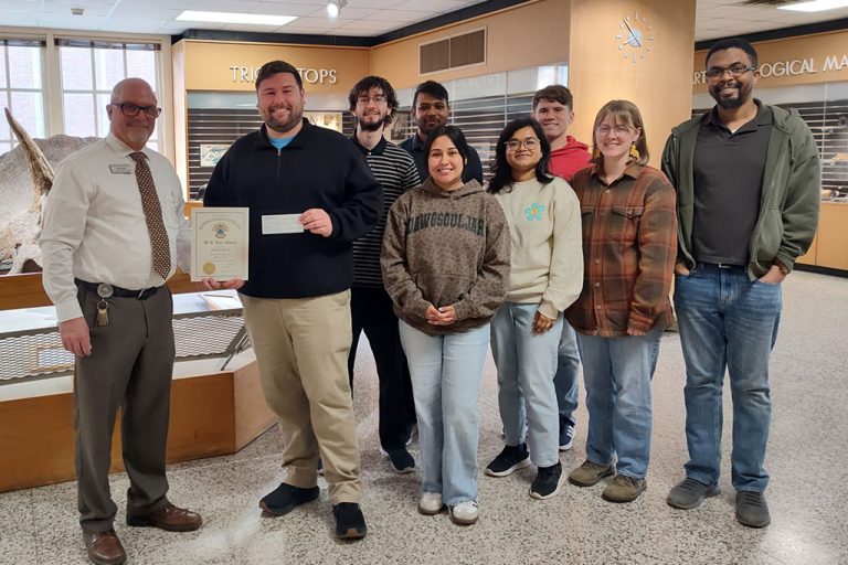 A group of people stands for a photo, centered around a student and staff member who holds up a certificate.