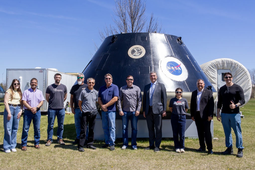 A group of 11 people stand in front of a space capsule relic located on the Univeristy of North Dakota's Inflatable Lunar-Mars Analog Habitat.