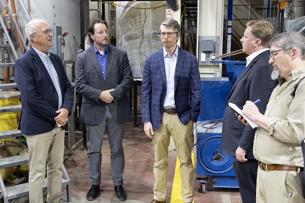 Five men stand inside the Drilling & Completions Laboratory near industrial equipment used for rare earth element research.