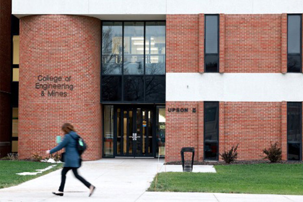 A student walks quickly in front of an entrance to the University of North Dakota College of Engineering & Mines.