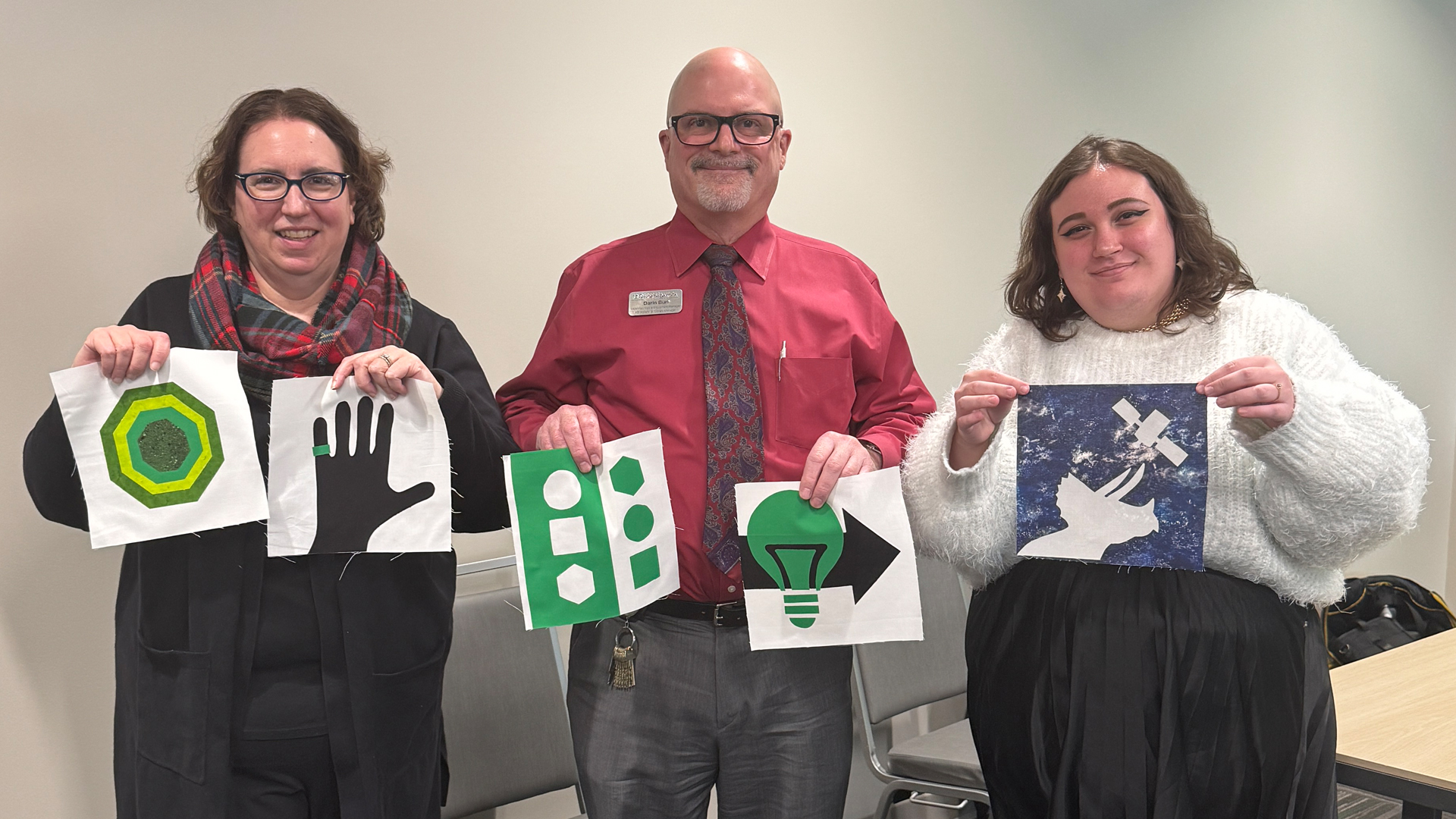 three people pose with partially completed quilt squares