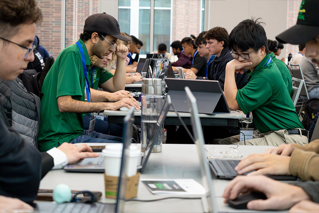 Students work diligently on laptops inside a ballroom.