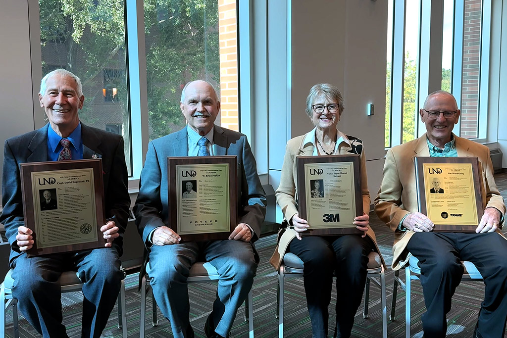 Four individuals hold plaques and sit next to one another for a group photo.