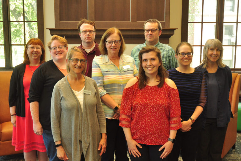 a group of 9 people in front of two large windows