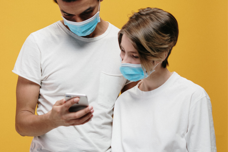 Two young people wearing masks looking at a cell phone