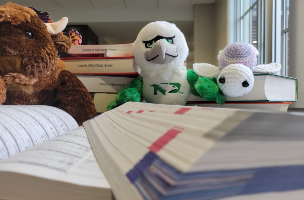 three plush animals surrounded by stacks of open library books