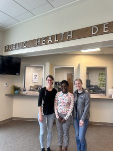 Mandy, Priscilla, and McKenna pose in front of the Public Health welcome desk.