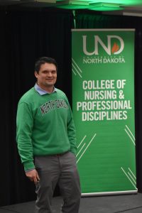 Dr. Nathaniel Johnson stands on stage with a green UND CNPD college banner behind him.