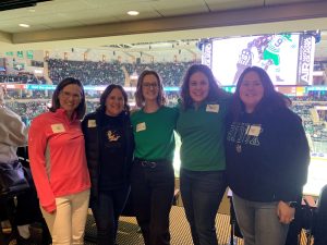 Five people, comprised of N&D faculty and alumni, stand in front of a UND Hockey Suite.