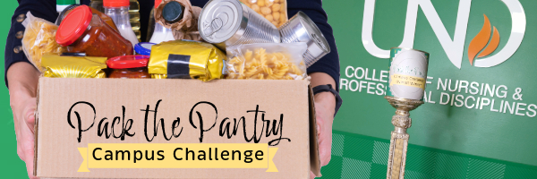 Person holding box of food, UND logo and Challenge Trophy in the background
