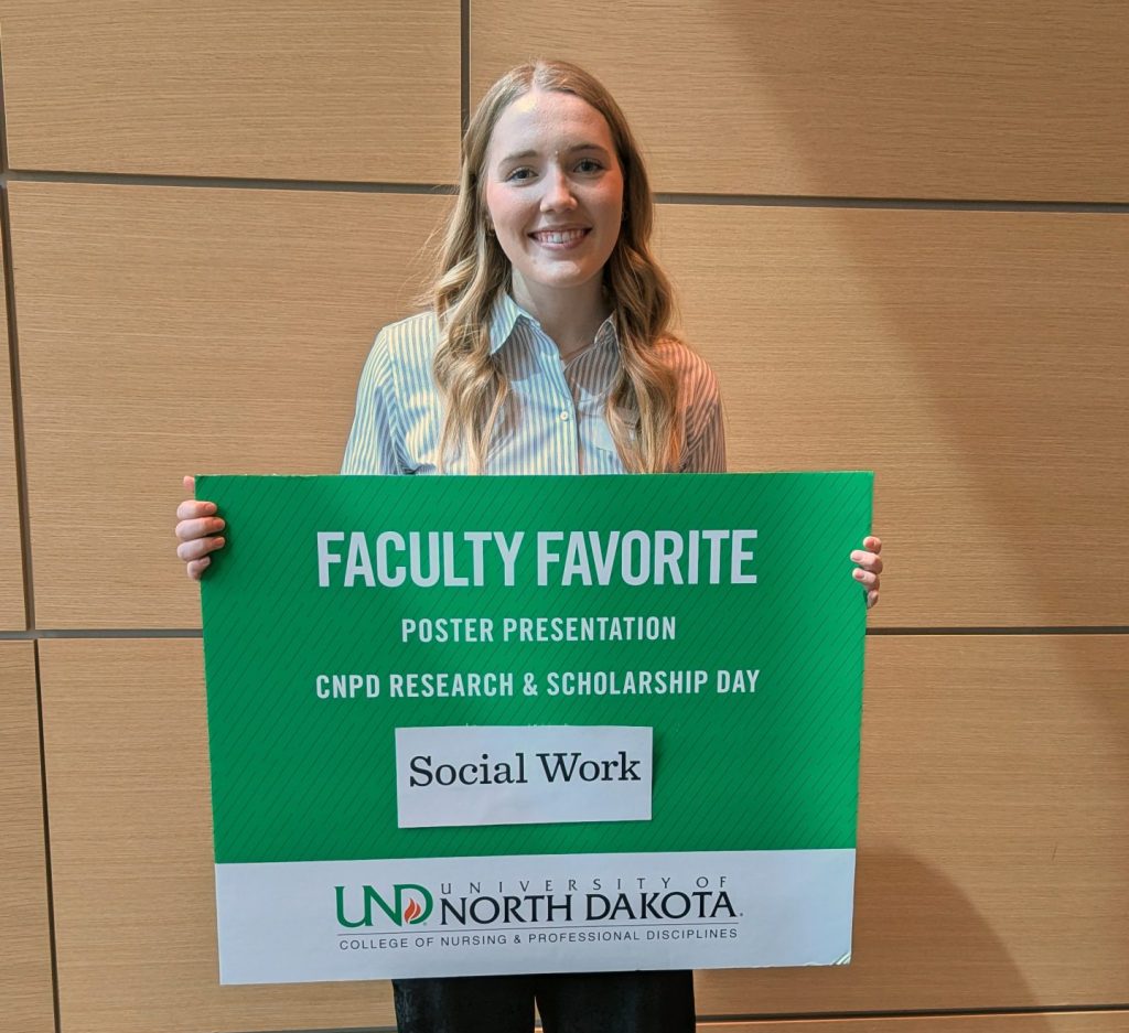 A social work student holds a green sign noting selection as faculty favorite.