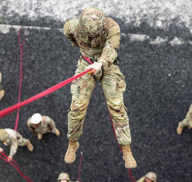 Cadet Hallberg rappels down a wall with a red rope strapped to a harness. snow dusts the ground below.