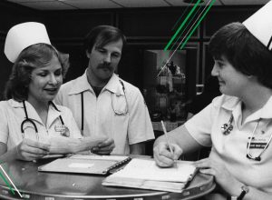 A black and white photo of nurses standing around a table.