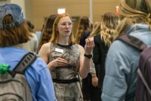 a student raises hands during a presentation of her poster to other attendees.