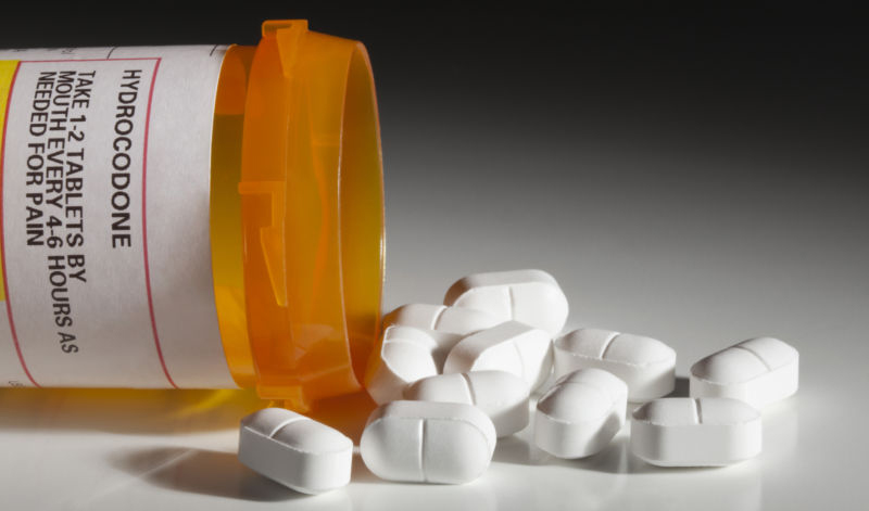 A bottle with a hydrocodone (the generic name for drug sold under other names by various pharmaceutical companies) label and hydrocodone tablets spilling out isolated on white background. Hydrocodone is a popular prescription semi-synthetic opioid that is used to treat moderate to severe pain. Hydrocodone is said to be one of the most common recreational prescription drugs in America.