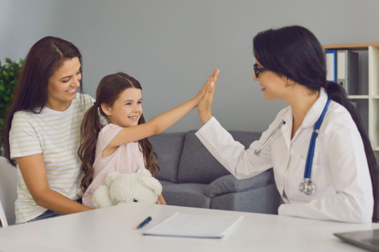 a person and a child sitting at a desk with a doctor. The doctor and child are giving high fives to each other