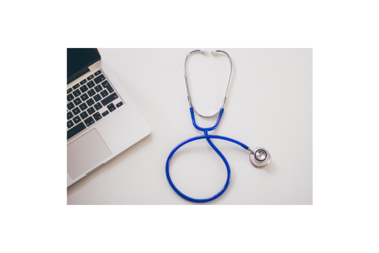 silver laptop with black keyboard on left side of a desk with blue and silver stethoscope on right