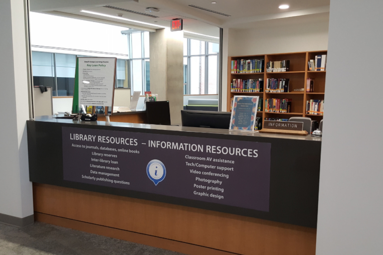 View of the information desk. There is a sig n on the front that lists "Library Resources" and services provided as well as "Information Resources" and services provided by that department.
