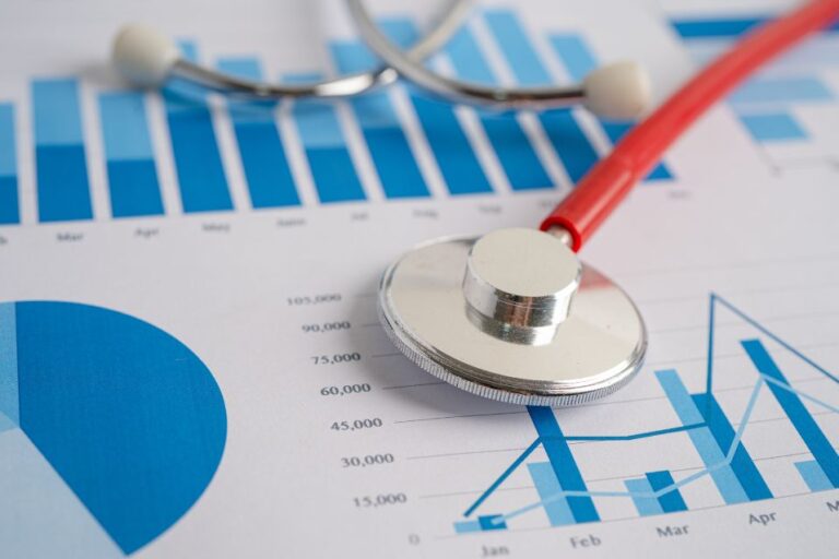a red and silver stethoscope sits on top of a statistics chart which is labeled by by a blue bar graph chart