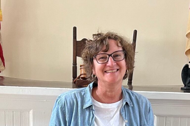 Allison sitting in a chair wearing a white shirt and blue jacket with a gavel behind her