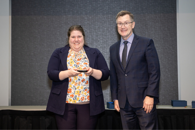 Sara Westall stands next to President Andrew Armacost while holding the Meritorious Service Award