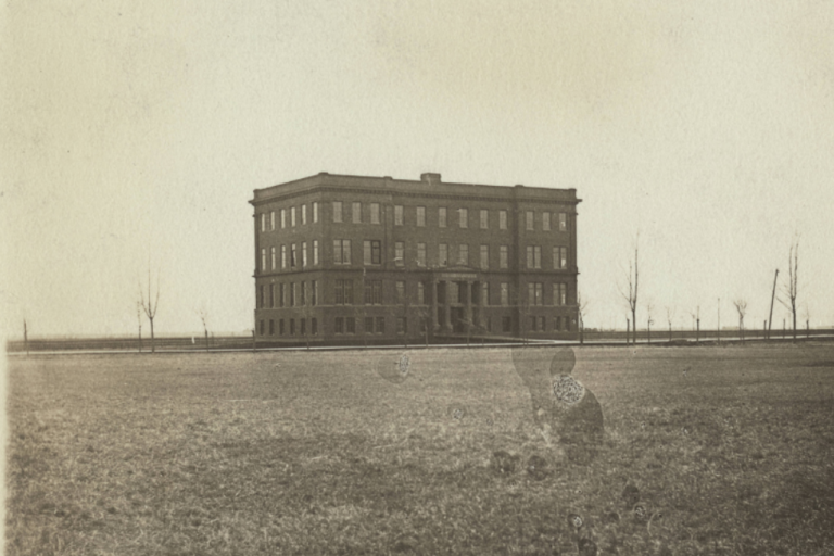 black and white photo of a rectangular four-story brick building with many windows on each floor and two small columns holding up a portico which reads "Science Hall".