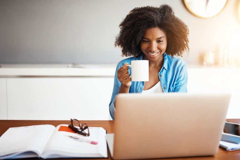Woman drinking coffee and looking at her computer screen with a smile on her face