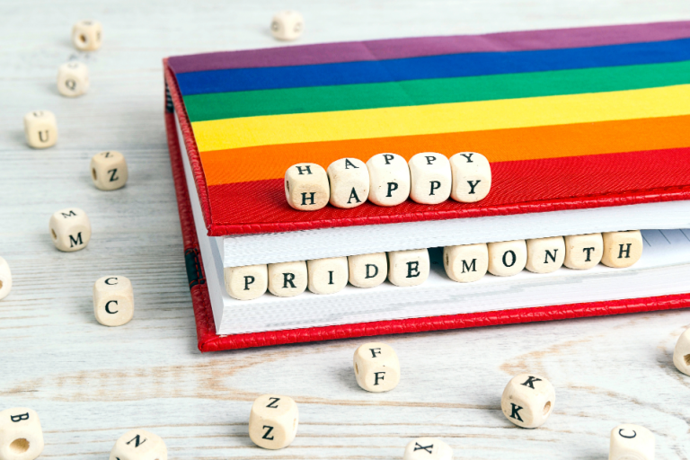 Book with rainbow colors and dice that spell out "happy pride month"