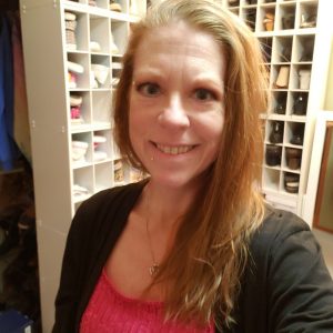 Amber McCann in a blazer and orange-pink shirt. She has collar-bone length copper hair.