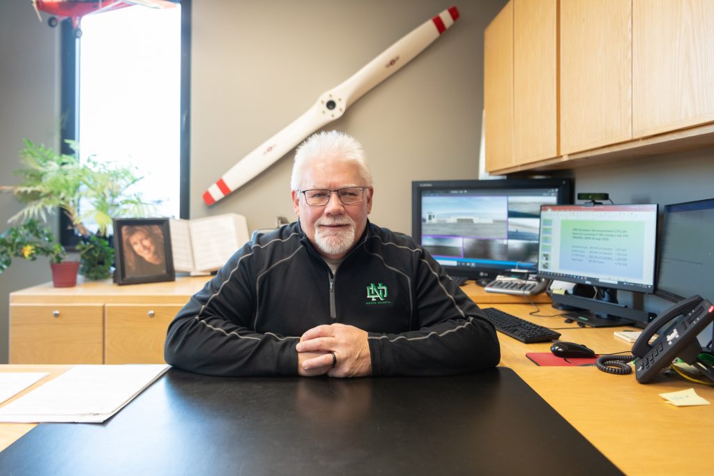 Dan Kasowski is pictured smiling with his hands crossed, sitting at a desk in his office.