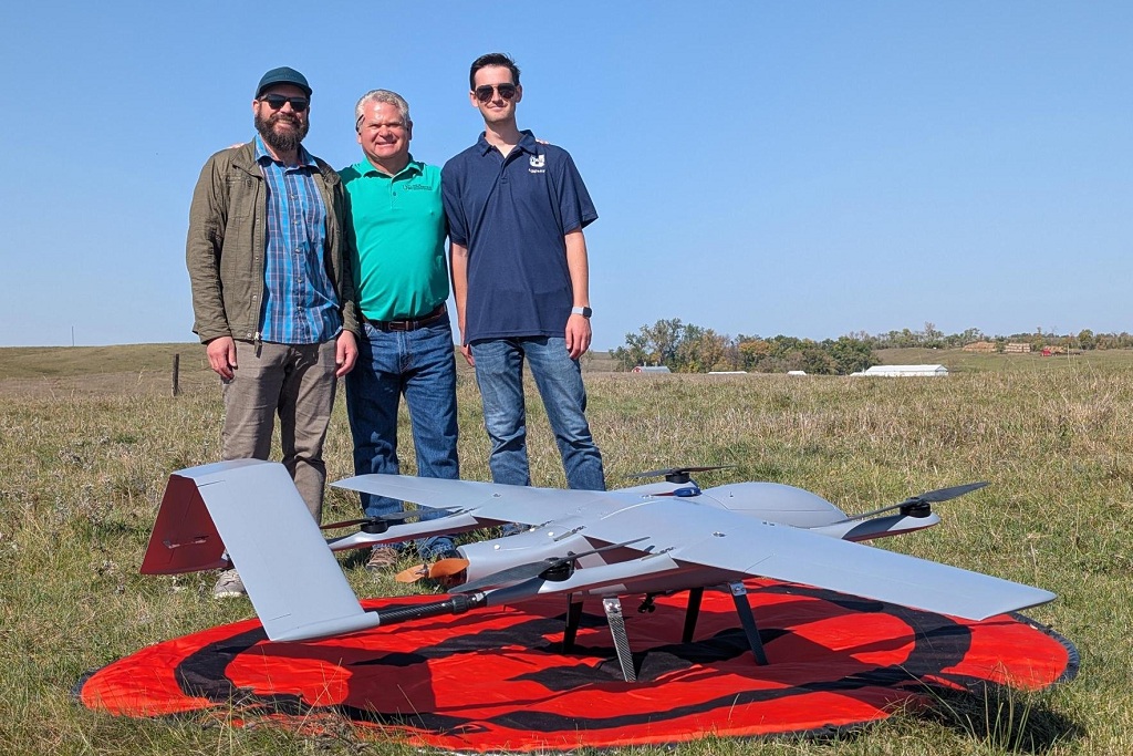  Cal Coopman, Jeff Barta, and Brandon Curdy stand by a drone in a field,