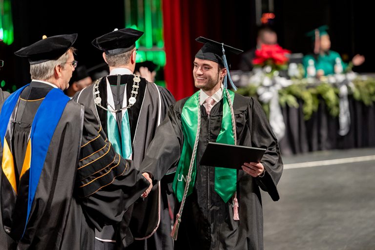 Student in commencement regalia shaking hands with professor after receiving degree