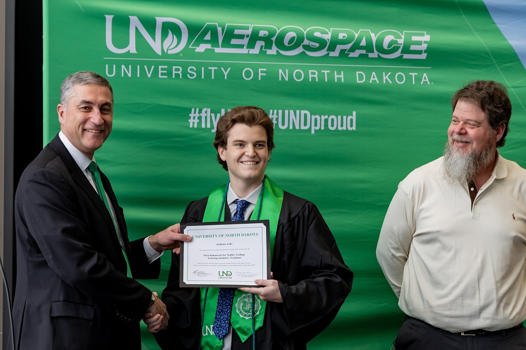 In a room on the UND campus, one man hands another a certificate while a third watches. 