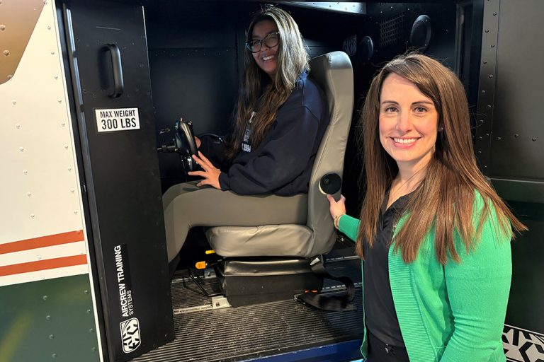 Jennifer Watne, right, stands next to a flight simulator, wherein UND student Megan Sung demonstrates the operatiion of the machine. Photo by Adam Kurtz/UND Today