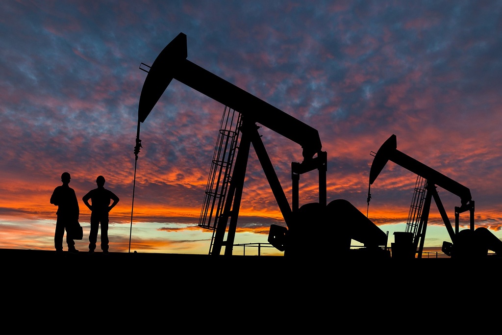 Two men stand by an oil pumpjack at sunset.