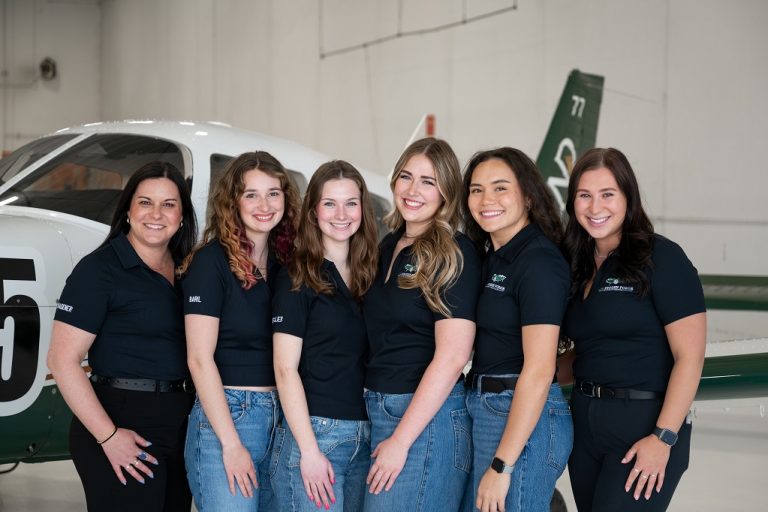 Two coaches and four members of the UND Frozen Force team stand by their UND aircraft in a hangar.