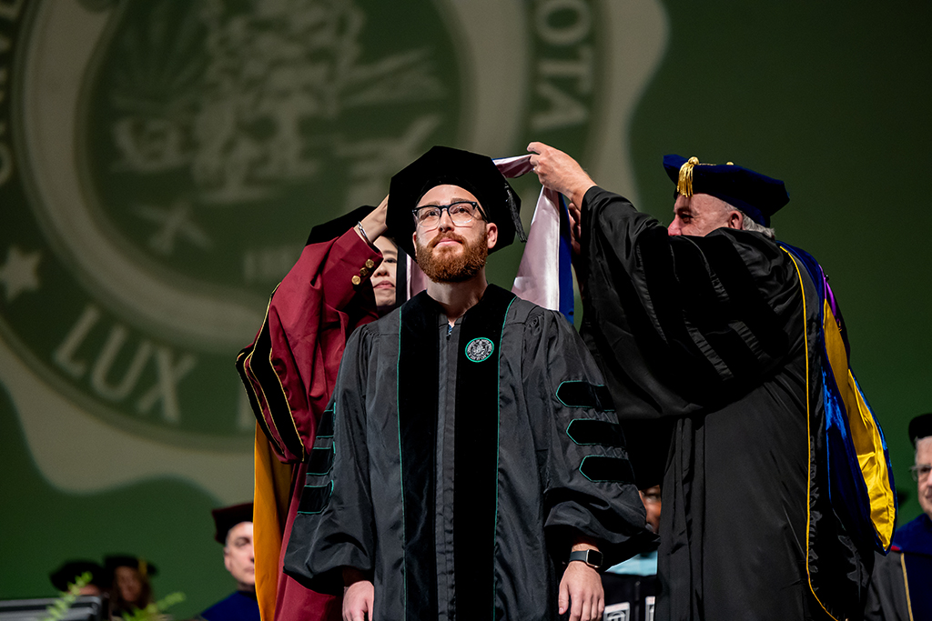 Student at graduation being hooded by two people wearing regalia