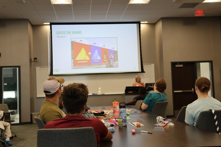 Speaker in front of classroom uses PowerPoint presentation to teach marketing to young people.