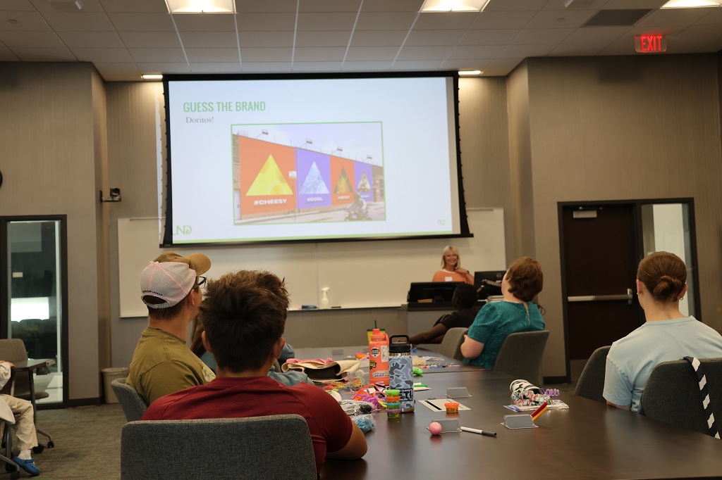 Speaker in front of classroom uses PowerPoint presentation to teach marketing to young people.
