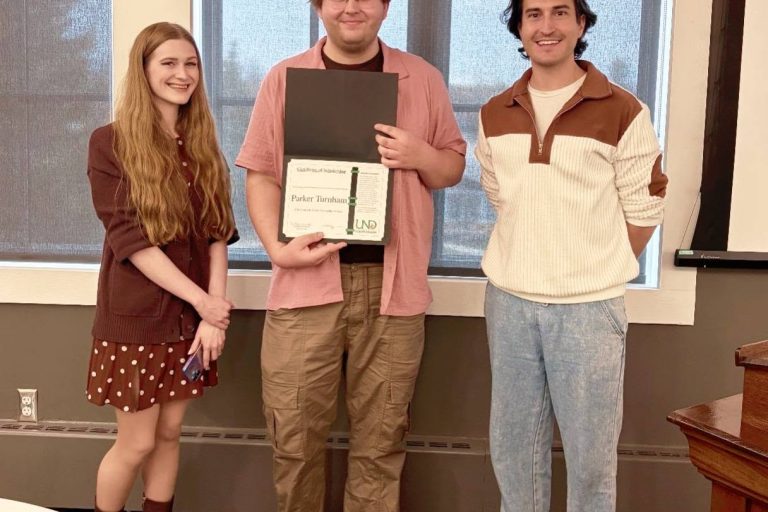 Three people standing in a row with the middle person holding a certificate.