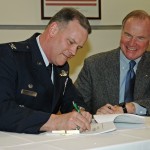 Col. Don Shaffer (left), commander of the 319th Air Refueling Wing at Grand Forks Air Force Base, signs a lease agreement that allows the University of North Dakota to use a facility on base for its unmanned aircraft systems (UAS) Center of Excellence. UND President Robert Kelley (right), who also signed the document, looks on.