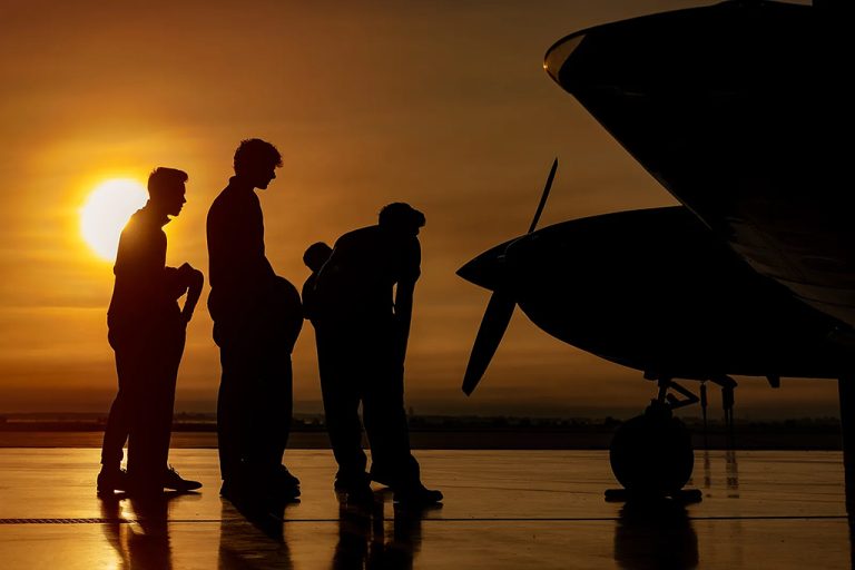 Silhouettes of three people examining nose of airplane against a sunset