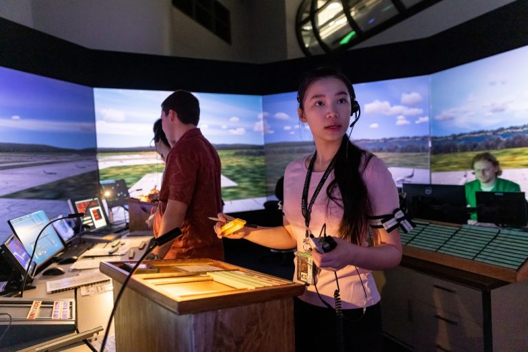 Students stationed in air traffic controller simulator, surrounded by screens displaying airfield.