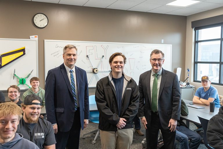 Greyson Orne standing between Andrew Armacost and Eric Link in classroom