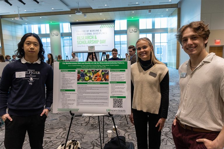 Three students stand next to research poster presentation