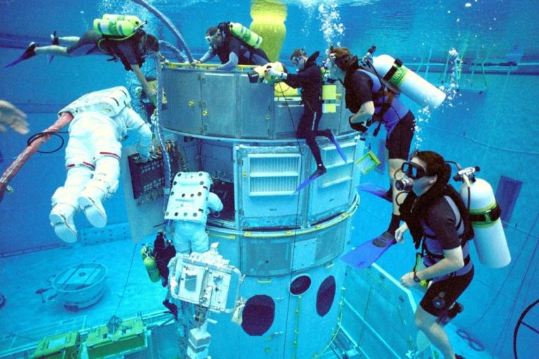 Team of divers and crew in astronaut suits submerged with capsule replica
