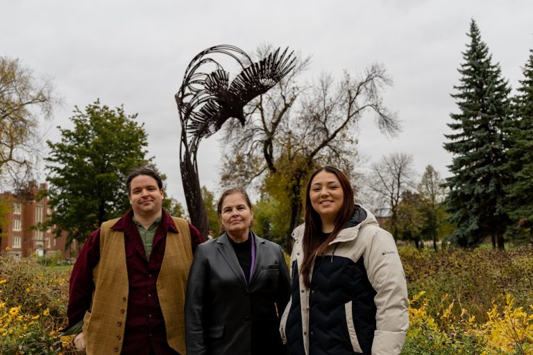 Three people stand in front of eagle sculpture on campus