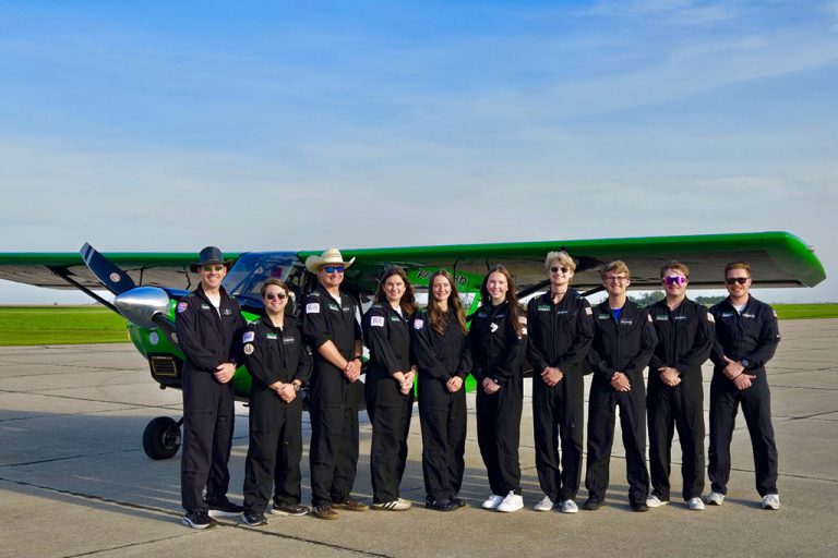 2025 UND Aerobatics team lined up for photo in front of UND-green airplane